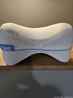 Side view of the white contoured leg and knee support pillow showing curved ergonomic shape.