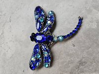 Top view showing detailed blue and white glass stones ornamenting the wings and body of the dragonfly brooch.
