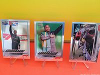 Three Lewis Hamilton trading cards displayed on stands showing him celebrating and his race car