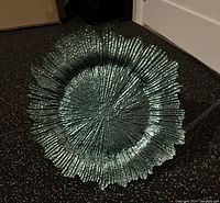 Teal centrepiece plate with textured pattern and petal-shaped edges placed on floor.