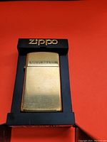 Solid brass Zippo lighter inside original black plastic frame with gold Zippo branding.