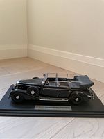 Side profile of black diecast 1938 Mercedes Benz 770k Pullman car on display base showing details of doors, wheels, and convertible roof.