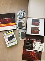 Wide angle photo showing all items in the lot including Traktor Scratch Pro 2 software box, two audio interfaces/adapters in blister packs, additional accessory boxes, and vinyl kit cards.