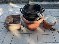 Assorted plant pots and tubs stacked together on tiled ground showing the types of gardening containers included in the lot.