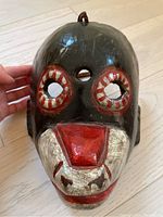 Front view of the wooden mask showing the painted eyes, snout-like mouth, and forehead hole.