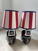Front view of two pirate-themed kids lamps with red and white striped lampshades and blue trim