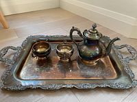 Tray with two pieces - creamer and coffee pot on a wooden floor, showing ornate details and patina