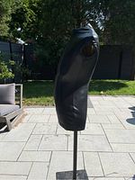 Side profile view of the black leather mannequin torso mounted on a metal stand outside.