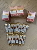 Front view of 4 boxes of L'Oreal Age Perfect Rosy Tone Moisturizer and 14 tubes of L'Oreal Age Perfect Radiant Serum Foundation arranged on floor.