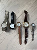 Five watches laid out flat, showing variety in bands and dial styles.