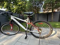 Full side view of white Giant Vandal 2.7 mountain bike with red front suspension fork and rear shock spring. Tires appear inflated but may need air or replacement. Shows used condition with dirt and wear.
