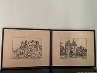 Two framed needlepoint artworks of castle scenes hung side by side on a wall