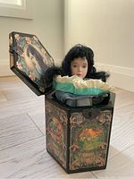 Side view showing the black octagonal box with delicate floral and fairy tale-themed painted panels and Snow White doll inside.