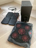 Photo showing computer subwoofer speaker, two laptop cooling pads on light wood floor