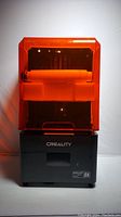 Front view of Creality Halot Mage 8K 3D printer with orange cover and black base displaying branding.
