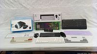 Lot showing multiple keyboards and gaming mice, various models visible in box and unboxed on table.