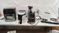 Four countertop appliances (air fryer, ice maker, juicer, toaster) on folding table