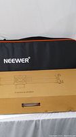 Closed brown box labeled 'Camera Slider' in front of a black and orange Neewer soft carrying case.
