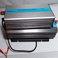 Top view of two power inverters stacked, showing Pooxtra model with label indicating power ratings and terminal clamps.