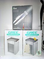 Two IQAir Atem personal air purifier boxes stacked on top of two Gree True HEPA air purifier boxes showing front product images and brand names.