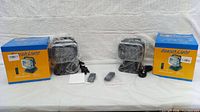 Two boxed black LED search lights wrapped in plastic with two remotes and power cables on white backdrop