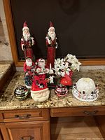 Photo of assorted Santa figures, Christmas-themed candles, and white poinsettia flower decoration arranged on a granite countertop.