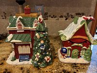 Front view of two ceramic Christmas-themed cookie jars, one a two-story house with a Christmas tree, the other a smaller house with candy cane decoration.