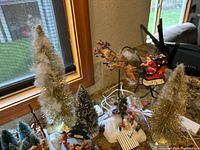 View of gold and white bottle brush trees along with suspended Santa sleigh and reindeer hanging ornament.