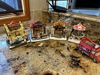 Front view of four Christmas carnival village decorations and red food truck on granite countertop