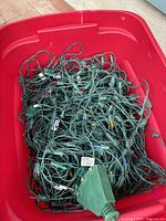 Green wire LED net lights coiled and placed in a red plastic bin, showing the power plug and wires.