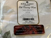 Tag on fabric indicating Royal Albert linens with Old Country Roses pattern, specifying 100% polyester napkin set.