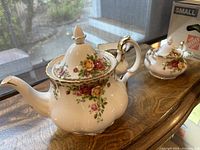 Front view of teapot, creamer and sugar bowl on wooden surface with window background
