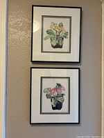 Two of the framed floral pictures, one with yellow flowers and one with pink flowers, hanging on a wall.