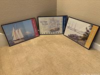 Three framed Tacoma Tall Ships items and one boxed wooden ship model kit grouped together on floor.
