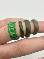Four green jade rings on finger, showing one ring with pierced carving and three smooth polished bands.