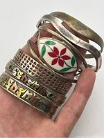 Close-up of stacked bracelets showing engraving, enamel inlay, and metal texture