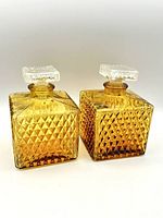 Front view of two square amber glass decanters with diamond textured sides showing clear glass stoppers on top.