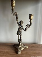 Front view showing the figurine holding two candle holders extending upward with leaf motifs and ornate base.