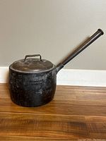 Side view of cast iron cooking pot showing full profile with lid and long handle.