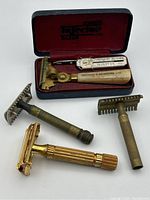 Four antique razors arranged with a Schick razor in original red velvet-lined case, and three other razors placed in front