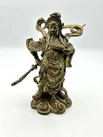 Front view of brass Asian warrior statue displaying detailed armor, facial features, and weapon with a swirling base.