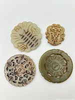 Top-down view of all four different carved Chinese hardstone pendants showing their shapes and carved details.