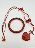 Full view of cinnabar bangle and matching necklace with carved pendant and beads laid flat on white background