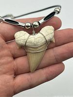 Close-up of the fossilized shark tooth pendant held in hand showing the wire wrapping and natural tooth details.
