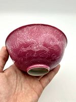 Pink Chinese dragon embossed porcelain bowl shown angled with underside visible in hand