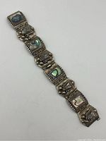 Front view of the vintage sterling silver abalone bracelet showing decorative linked panels with abalone shell inlays and ornate silver details, bracelet broken halfway.