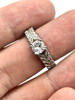 Close-up of the ring on finger showing the main cubic zirconia and leaf design on the band