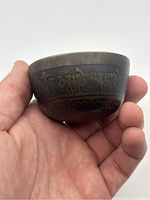 Photo showing side view of the small bronze bowl with Tibetan script engraved around the outer side near rim