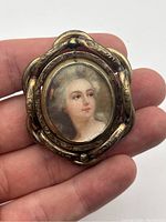 Brooch held in hand showing size and detailed portrait of a Victorian lady.