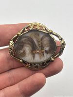 Front and angled view showing the woven hair strands preserved under glass with gold wire detail and ornate gold fill frame.